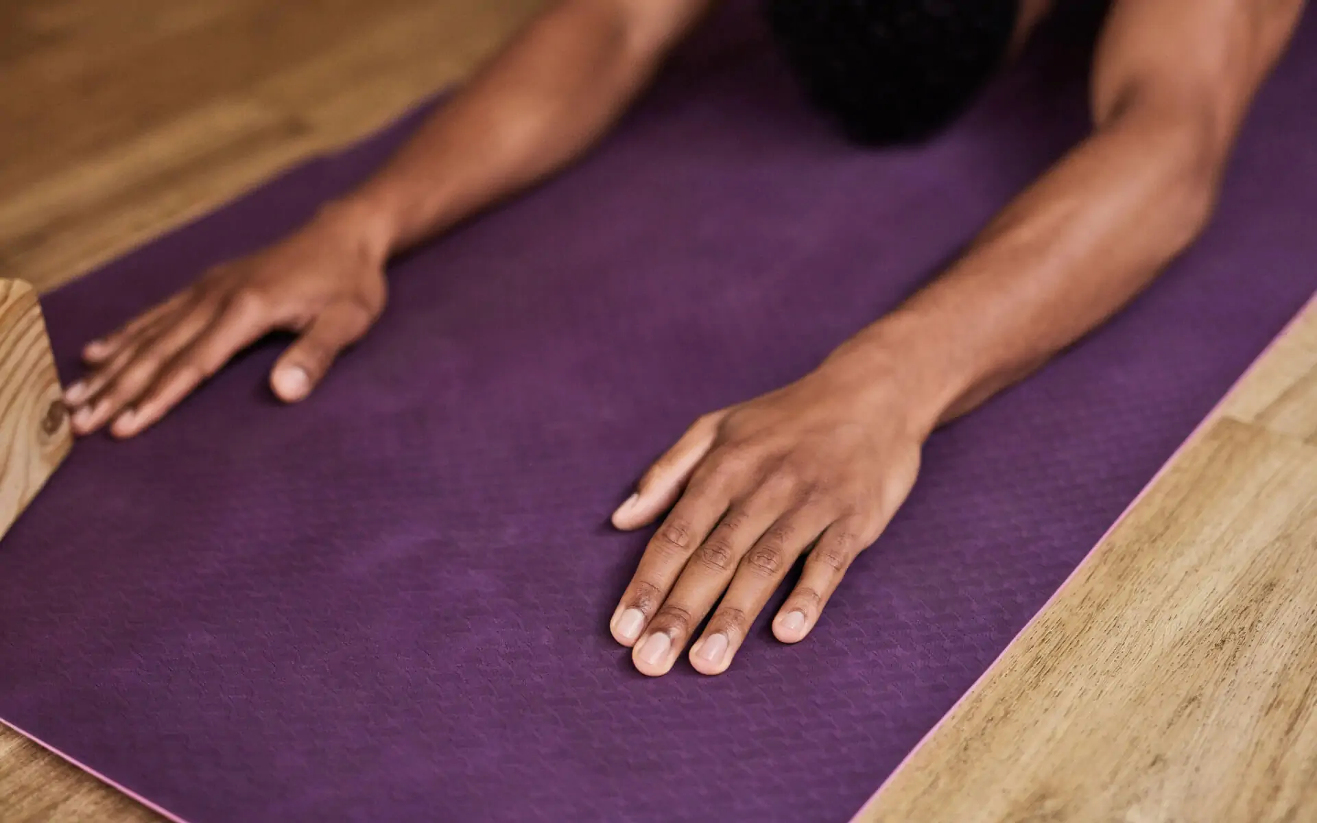 Woman's hands on a purple yoga mat, in a position of devotion, self-care and rest 