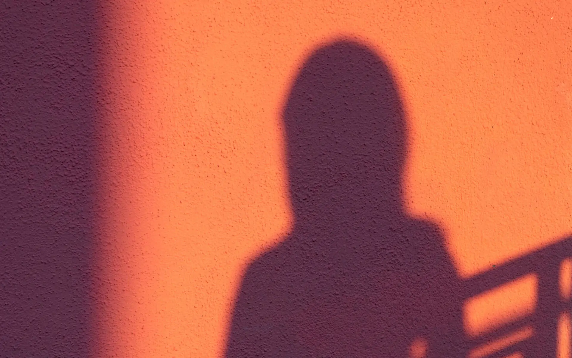 Shadow of a woman projected on an orange wall used to symbolize the parts of ourselves we can't see.
